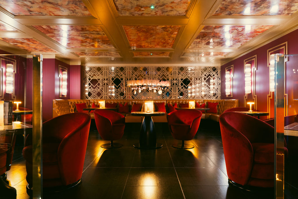 An empty lounge with red velvet armchairs beneath a gilded ceiling